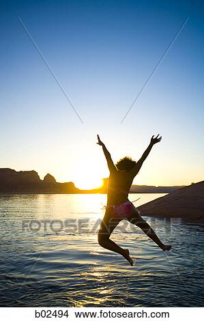 Picture - Rear view of a young woman jumping into a lake. Fotosearch