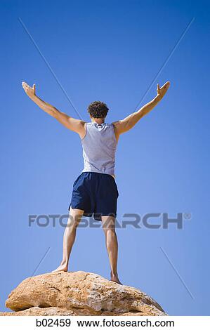 Low angle view of a young man standing on a rock with his arm outstretched View Large Photo Image Stock Photo - Low angle view of a young man standing on a rock with his arm outstretched. Fotosearch