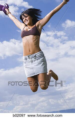 Low angle view of a young woman holding her top and jumping View Large Photo Image Stock Photo - Low angle view of a young woman holding her top and jumping. Fotosearch