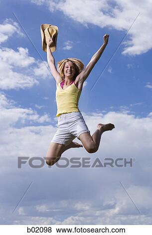 Low angle view of a young woman holding her hat and jumping View Large Photo Image Stock Photo - Low angle view of a young woman holding her hat and jumping. Fotosearch