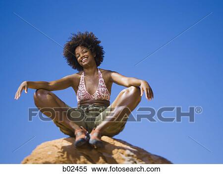 Low angle view of a young woman sitting on a rock View Large Photo Image Stock Photography - Low angle view of a young woman sitting on a rock. Fotosearch