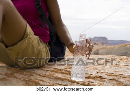 Stock Image - Mid section view of a young woman holding a water bottle. Fotosearch
