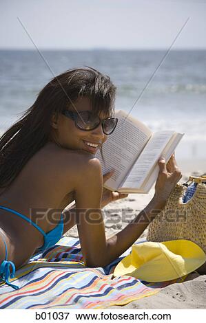 Stock Photo - Rear view of a young woman reading on the beach. Fotosearch