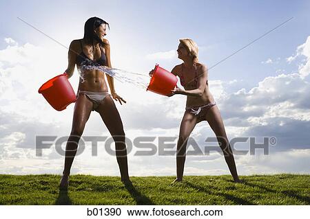 Two young women throwing water at each other View Large Photo Image Stock Image - Two young women throwing water at each other. Fotosearch