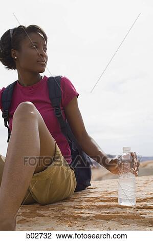 Young woman sitting on a rock holding a water bottle View Large Photo Image Stock Image - Young woman sitting on a rock holding a water bottle. Fotosearch