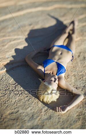 Stock Image - High angle view of a young woman lying on a rock. Fotosearch