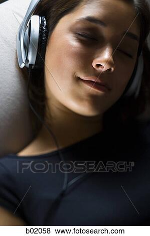 Stock Photo - High angle view of a young woman listening to music on headphones. Fotosearch