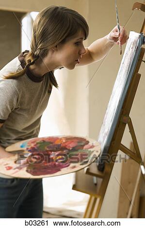 Stock Image - Profile of a young woman painting on a canvas. Fotosearch
