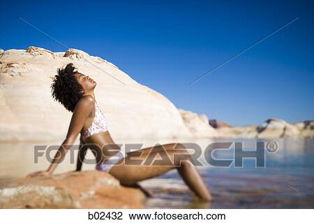 Stock Image - Profile of a young woman sitting on a rock with her eyes closed. Fotosearch