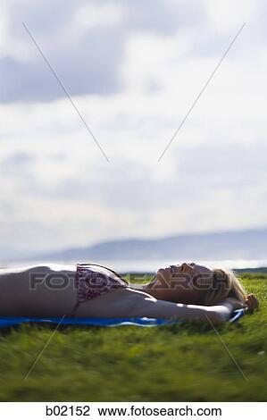 Young woman lying down on a field View Large Photo Image Stock Image - Young woman lying down on a field. Fotosearch