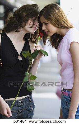 Picture - Two teenage girls smelling a rose. Fotosearch