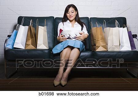 Young woman sitting on a couch with shopping bags View Large Photo Image Stock Photo - Young woman sitting on a couch with shopping bags. Fotosearch