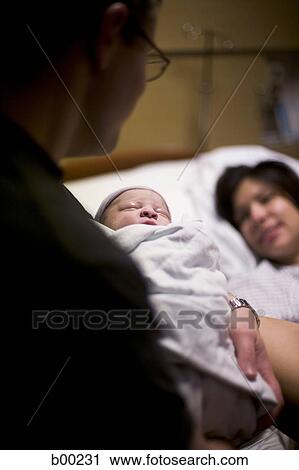 Father carrying his newborn baby girl with his wife lying on a bed View Large Photo Image Stock Image - Father carrying his newborn baby girl with his wife lying on a bed. Fotosearch
