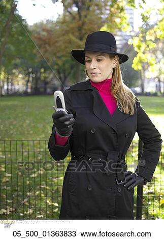 Stock Image - Woman, Spring, Phone, Park, raincoat, coat, hat. Fotosearch