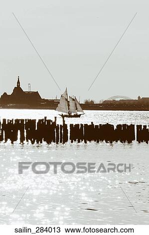 Stock Image - A landscape of a sailboat drifting through a harbor.. Fotosearch