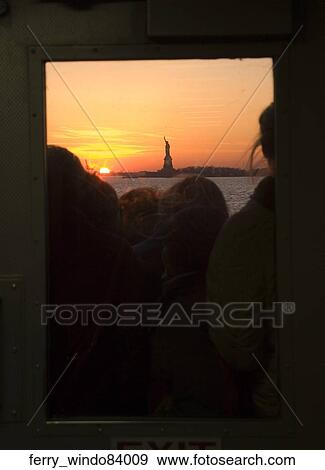 Stock Photo - Passengers look at the Statue of Liberty, back lit from a golden sunset, outside a ferry window.. Fotosearch