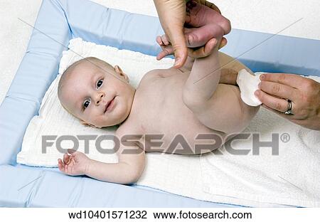 Stock Image - A baby lying on a changing table looking up having its bottom wiped and nappy changed.. Fotosearch
