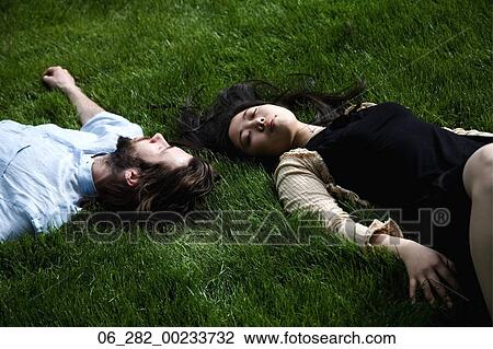 Stock Image - Above view head and shoulders couple lying on grass with their eyes closed. Fotosearch