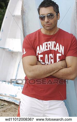 Stock Photo - Brunette male leaning against a boat wearing a red logo print T shirt. Fotosearch