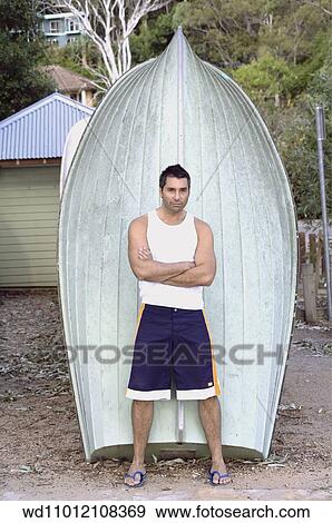 Stock Photo - Brunette male leaning back against a boat wearing a white T shirt. Fotosearch