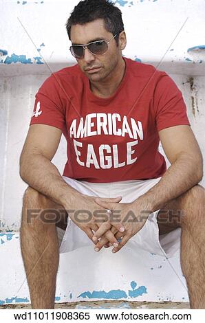 Stock Photography - Brunette male sat down wearing a red logo print T shirt. Fotosearch