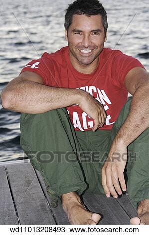 Stock Image - Brunette male wearing a red logo T shirt and green combat trousers. Fotosearch