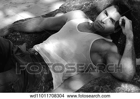 Brunette male wearing a white vest lying back on a rock View Large Photo Image Picture - Brunette male wearing a white vest lying back on a rock. Fotosearch