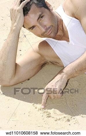 Stock Photo - Brunette male wearing a white vest lying on the beach. Fotosearch
