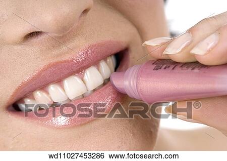 Stock Photograph - Close up of female applying pink lipgloss smiling showing teeth.. Fotosearch