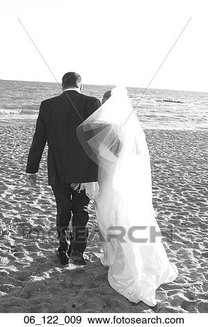Stock Photo - couple outside happy wedding 20's 30's kiss kissing veil silhouette love lovers marriage partnership white dress beach walking ocean sea man woman portrait. Fotosearch