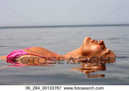 Stock Photo - Half length side view woman floating on water in a pink bikini with head back and eyes closed. Fotosearch