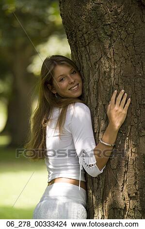 Half length side view young woman long blonde hair standing holding a tree trunk looking at camera smiling View Large Photo Image Picture - Half length side view young woman long blonde hair standing holding a tree trunk looking at camera smiling. Fotosearch