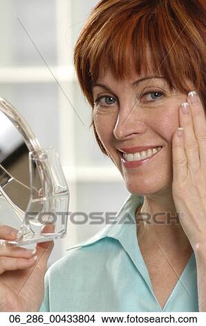 Head and shoulders front view portrait woman holding a hand mirror looking at camera smiling View Large Photo Image Picture - Head and shoulders front view portrait woman holding a hand mirror looking at camera smiling. Fotosearch