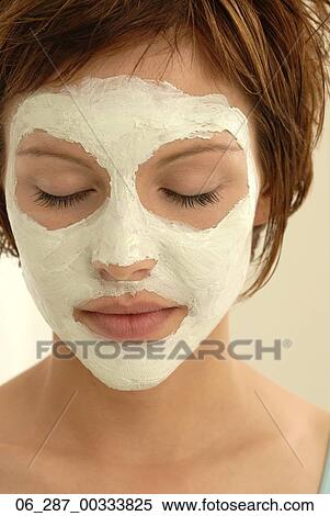 Stock Photography - Head and shoulders front view portrait young woman in a face mask looking down with eyes closed. Fotosearch