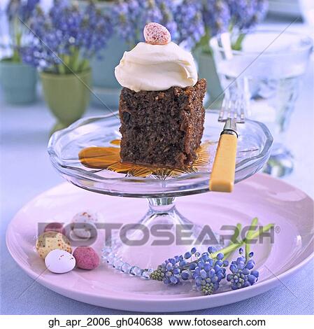 Stock Photo - Spiced carrot and walnut puddinng with dollop of fresh cream on top on glass cake stand. Chocolate mini easter eggs on the side of plate.. Fotosearch