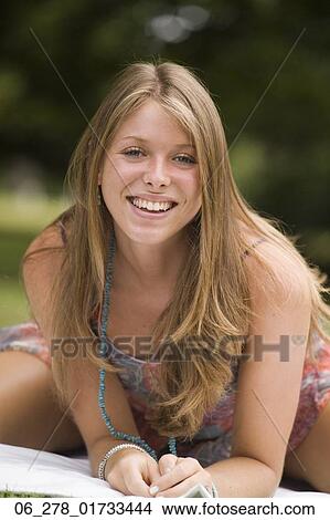 Picture - Three quarter length front view young woman long blonde hair leaning forward on elbows looking at camera smiling. Fotosearch