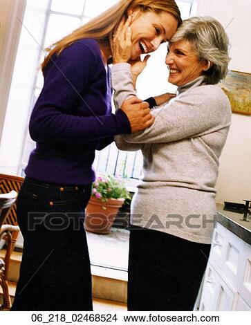 Picture - woman portrait mother couple family happy smiling affectionate hugging winter inside laughing embrace sweater trouser skirt black blue blonde grey hair. Fotosearch