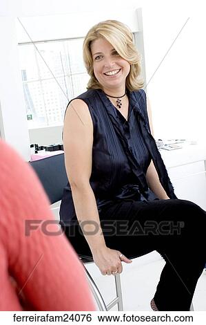 A blonde woman in her 30's wearing a navy blue shirt sitting on a chair in front of a window. View Large Photo Image Stock Photograph - A blonde woman in her 30's wearing a navy blue shirt sitting on a chair in front of a window. . Fotosearch