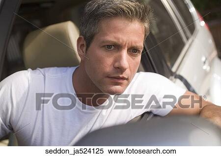 A man wearing a white t-shirt sitting in a car experiencing road rage. View Large Photo Image Stock Photography - A man wearing a white t-shirt sitting in a car experiencing road rage.. Fotosearch
