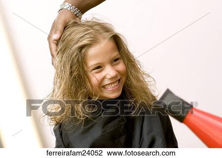Stock Image -  A young girl having her hair styled with a red hair dryer at a salon.. Fotosearch