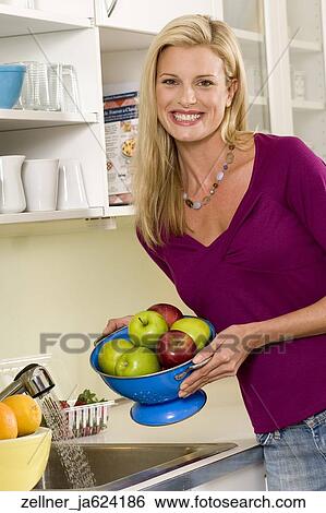 Stock Photograph -  Blonde female in her 30's holding a bowl of apples in a kitchen.. Fotosearch