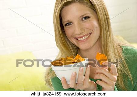 Blonde woman in her 20's holding a bowl eats potato chips View Large Photo Image Stock Photo - Blonde woman in her 20's holding a bowl eats potato chips. Fotosearch