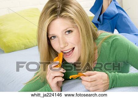 Blonde woman in her 20's lying on a bed eats potato chips. View Large Photo Image Stock Photograph - Blonde woman in her 20's lying on a bed eats potato chips.. Fotosearch