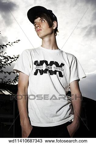 Stock Image - Brunette male teenage boy standing outdoors looking to the side wearing a white T shirt and a black baseball cap. Fotosearch