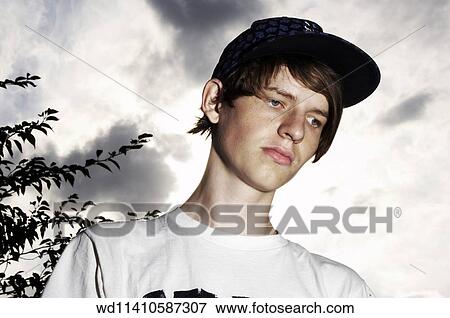 Stock Photo - Brunette male teenage boy standing outdoors looking to the side wearing a white T shirt and a black baseball cap. . Fotosearch