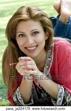 Stock Image -  Brunette woman poses in a park lying on her stomach.. Fotosearch