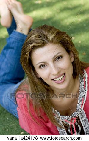 Stock Photo -  Brunette woman poses in a park lying on her stomach. Fotosearch