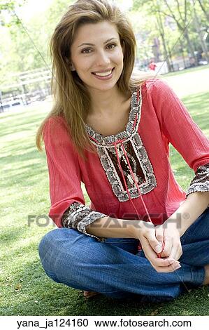 Stock Image -  Brunette woman poses in a park sitting on the grass.. Fotosearch
