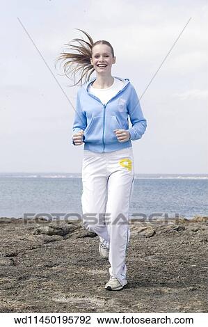 Female with long blonde hair off face wearing blue hooded top and white t shirt with white tracksuit trousers and trainers running towards camera with sea in background smiling showing teeth. View Large Photo Image Stock Image - Female with long blonde hair off face wearing blue hooded top and white t shirt with white tracksuit trousers and trainers running towards camera with sea in background smiling showing teeth.. Fotosearch