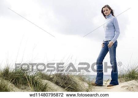Female with long blonde hair wearing pale blue poloneck jumper and blue jeans standing on sand dune with sea in background View Large Photo Image Stock Image - Female with long blonde hair wearing pale blue poloneck jumper and blue jeans standing on sand dune with sea in background. Fotosearch
